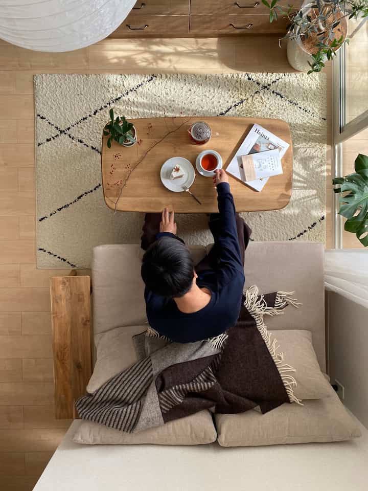 明るい木目調の北欧リビング、ベージュのソファと植物、ホームカフェの小物が配置された雰囲気のある空間