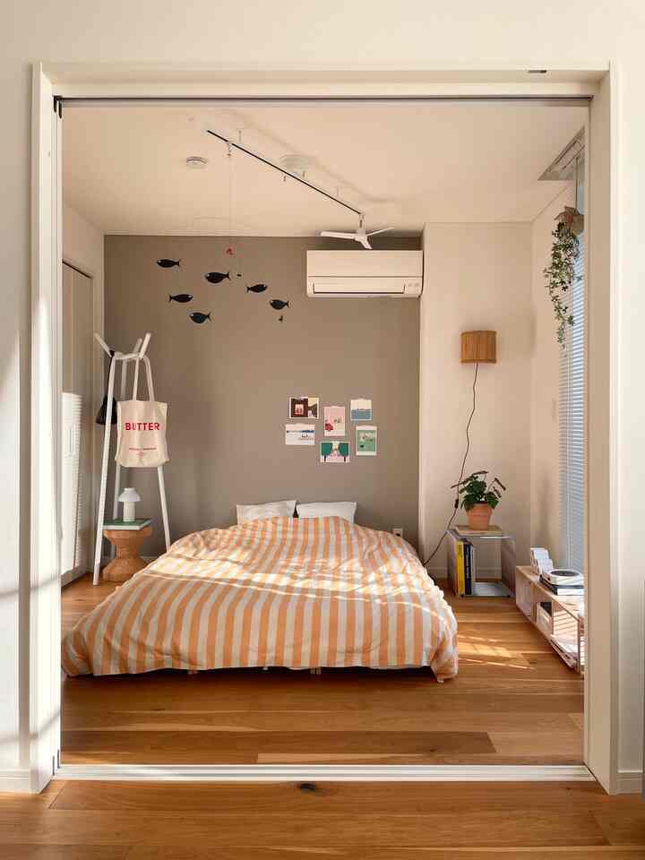 温かみのある木目調とナチュラル素材が印象的な北欧風の寝室、中央にオレンジのストライプベッドカバーとモビールが配置された空間