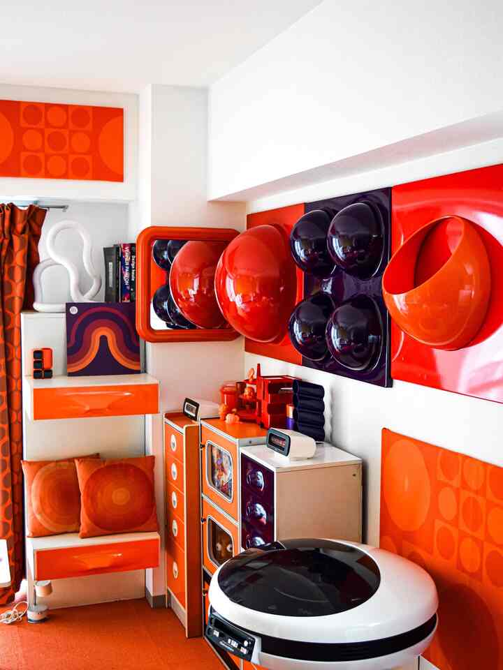 Retro living room in vivid orange and red tones, featuring geometric wall art and space-age decor with compact layout