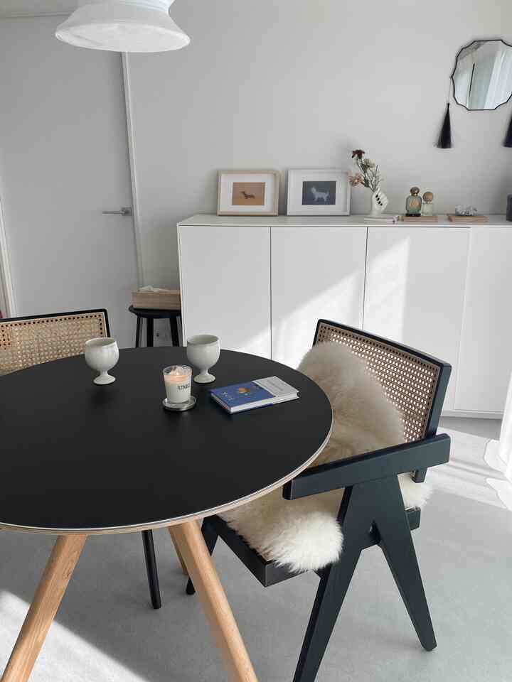 A simple and modern dining space with white walls, black round dining table with wood legs, and a black dining chair