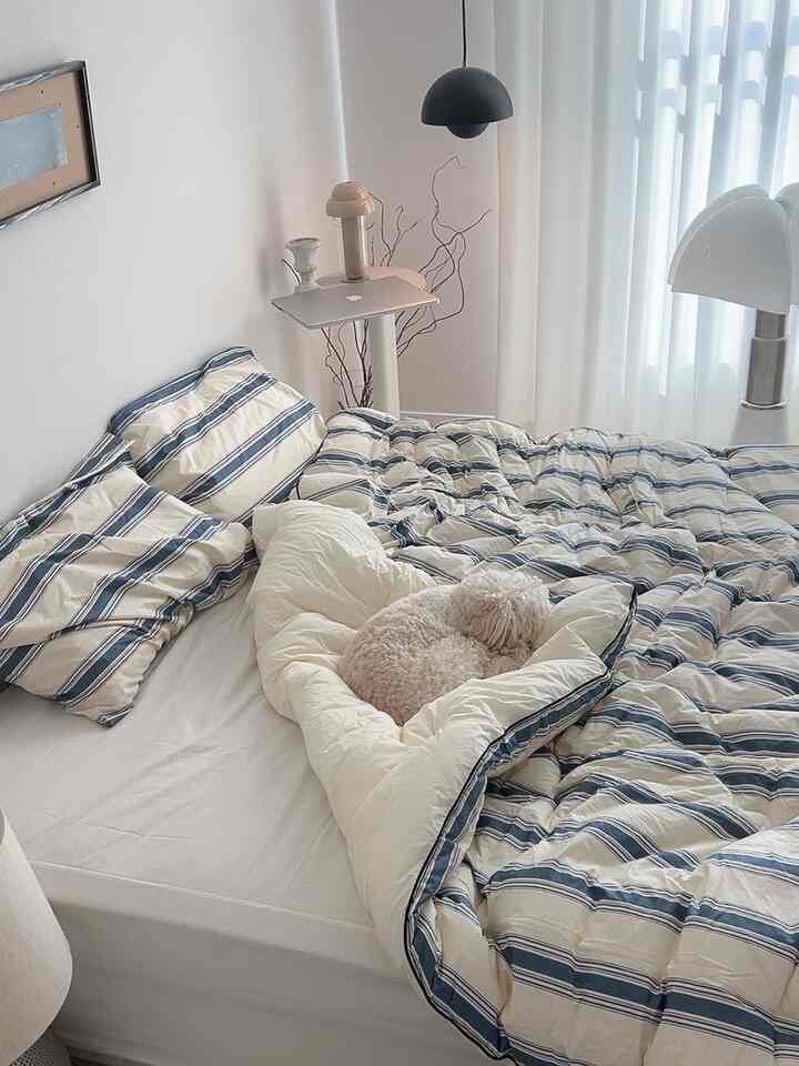 Natural toned bedroom featuring a striped bedspread and a white dog resting, creating a cozy atmosphere
