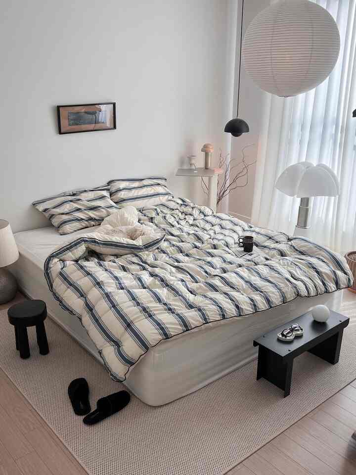 白を基調とした寝室、ネイビーストライプの寝具とシンプルなサイドテーブルが配置されたモダンな雰囲気のインテリア