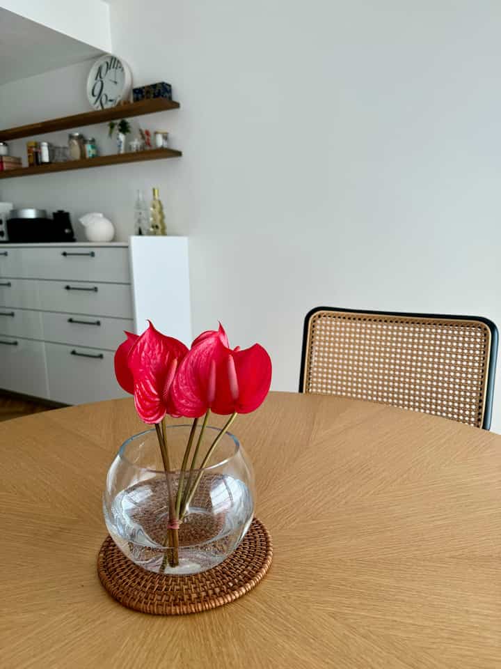 Natural color kitchen and dining table space featuring a clear vase with red flowers in a natural modern vibe