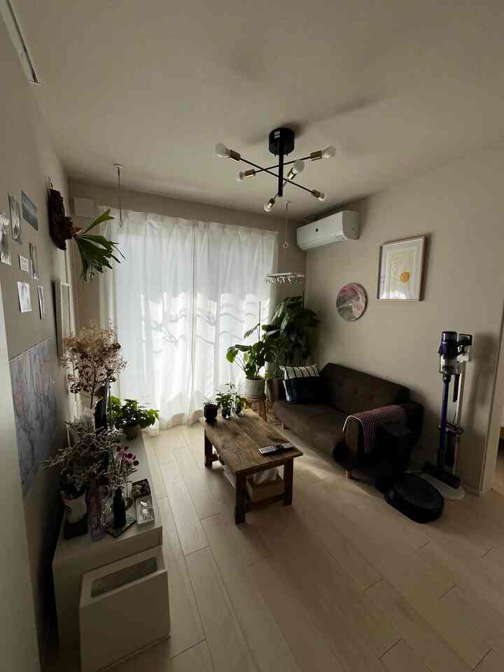 明るいホワイトトーンのコンパクトなリビング、ダークブラウンのソファと木製ローテーブル、多数の植物を配したナチュラルな北欧風インテリア