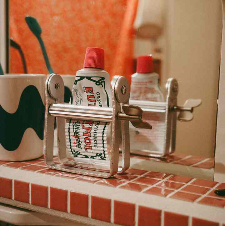 赤とベージュの浴室タイルの上にステンレスのチューブ絞り器、歯磨き粉、歯ブラシが置かれた雰囲気あるバスルーム