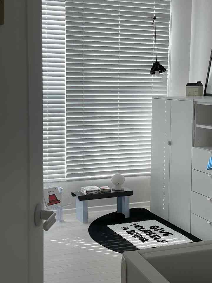 Natural tone living room in white and black featuring window blinds, a small bench, and a rug in a simple and clean space