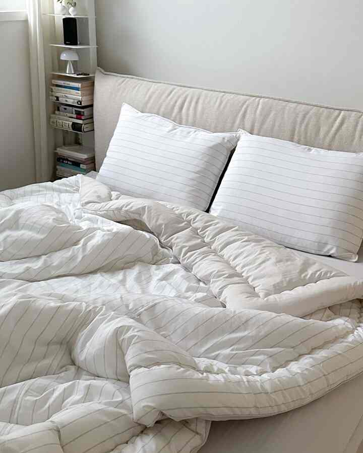 白とベージュの寝室、枕とストライプの掛け布団カバーが配置されたシンプルでナチュラルな雰囲気のインテリア