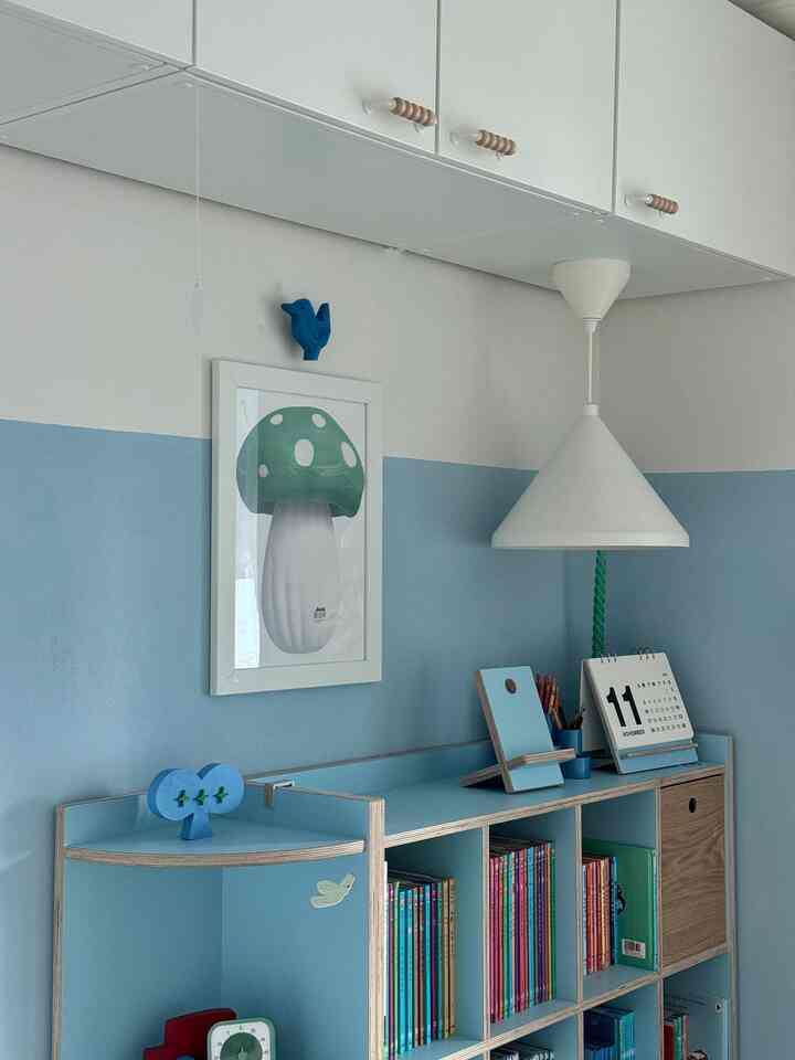 Kids' room with blue wall and white overhead storage, featuring a mushroom poster and bookshelf in a neat study area