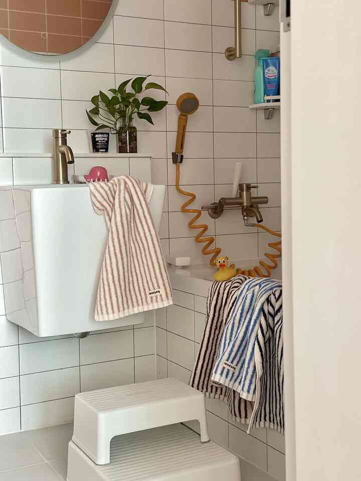 White tiled bathroom featuring step stool and a cute rubber duck, creating a child-friendly bathing space