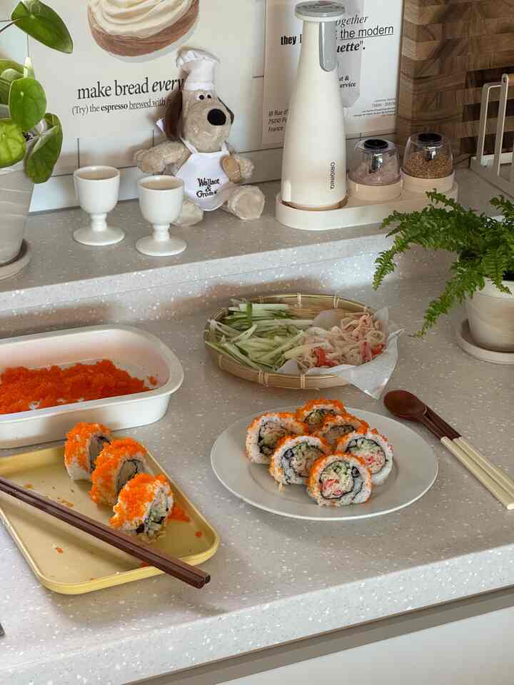 白いトーンのキッチンにキッチン用品と皿の上のおいしそうなカリフォルニアロールが配置された、雰囲気のあるホームクッキングスペース