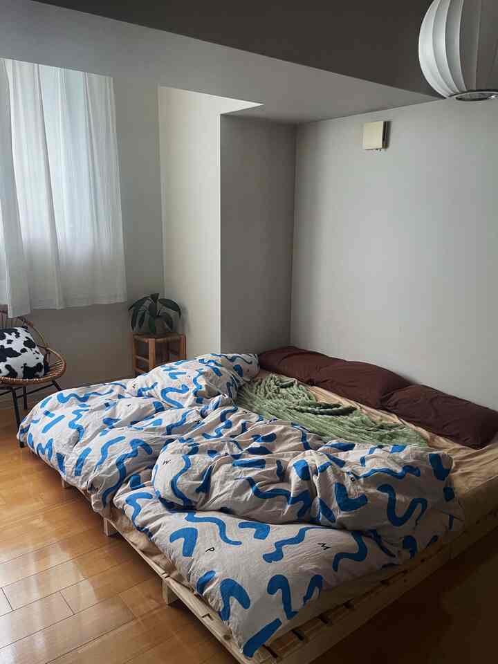 ナチュラルな色調の寝室、パレットベッドとグリーンのブランケット、青い模様の掛け布団カバーが配置された落ち着いた空間。