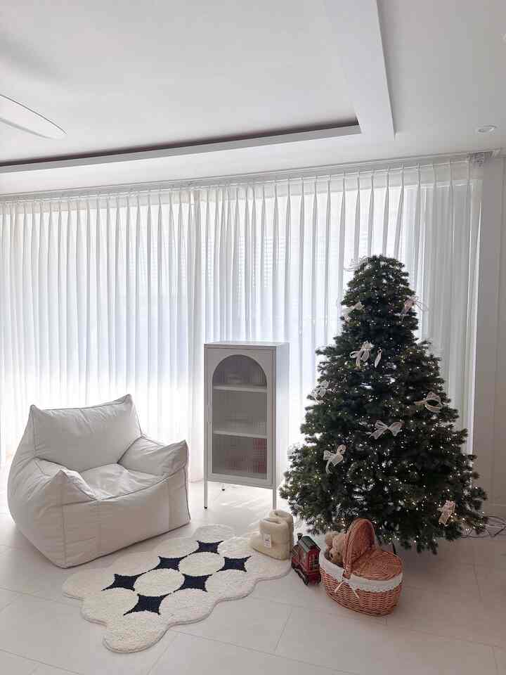 Bright white and beige toned living room featuring a Christmas tree, a bean bag sofa, a metal storage cabinet, and a mini rug, creating a cozy atmosphere