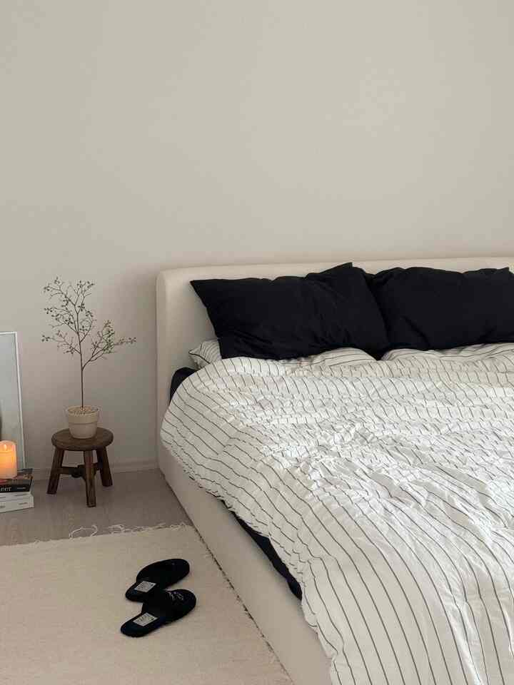 White and black themed bedroom featuring a large bed with striped bedding, accented by a natural wood stool and potted plant creating a cozy atmosphere