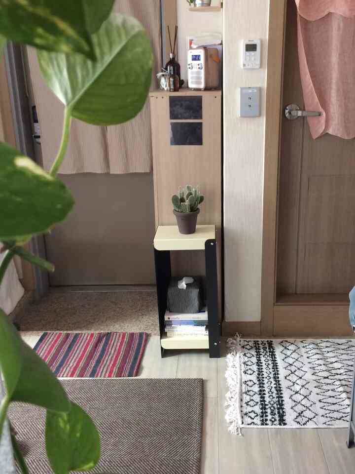 ベージュとブラックのトーンの狭い玄関スペース、コーナーに収納棚と複数のラグが配置された雰囲気のあるインテリア