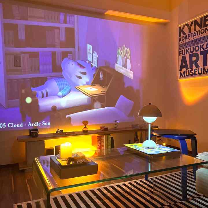 暖かい黄色の照明が灯るミッドセンチュリーモダンのリビング、透明なガラステーブルとプロジェクターが配置された雰囲気のあるインテリア