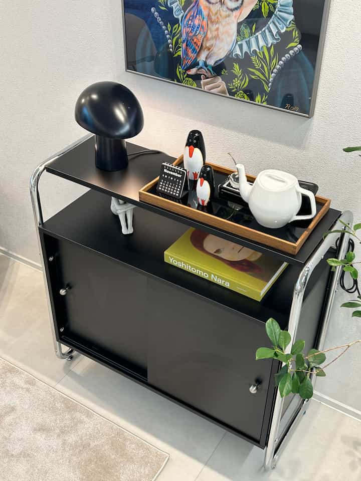 黒いコンソールキャビネットの上にオブジェとティーポットが置かれ、壁に鳥のアートが飾られた洗練された空間