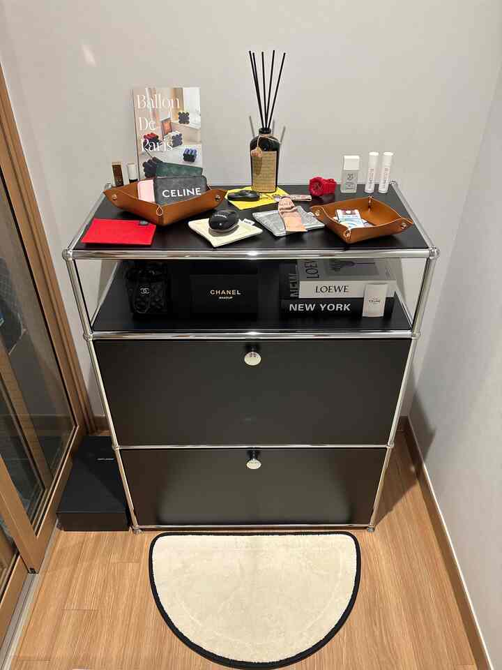 ベージュの木目調フロアとブラックの収納が置かれた狭い玄関スペース、トレイやディフューザーなどの小物が整った雰囲気のあるインテリア