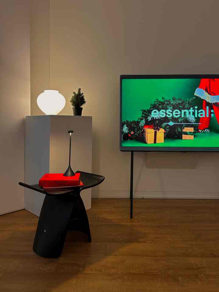 Modern living room with white pedestal and wood tone flooring, featuring a black stool and accent lighting in a sleek interior
