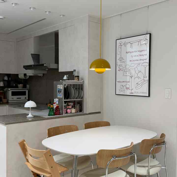 A clean and natural 20-pyeong new apartment dining area featuring a white and wood-toned table and chairs, highlighted by a yellow pendant light