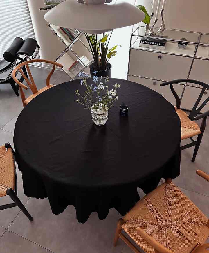 黒いテーブルクロスがかかった丸いダイニングテーブルと木目調の椅子、中央に花瓶が配置されたモダンなダイニングルーム