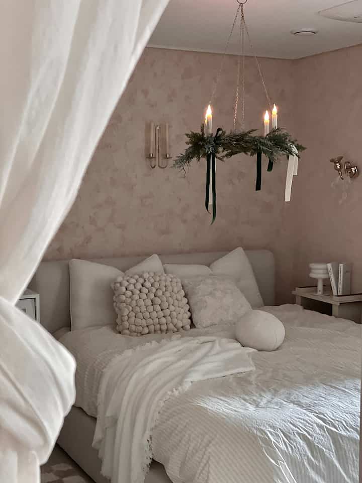 Neutral-toned bedroom featuring a large bed with cushions and a hanging wreath, creating a cozy, soft atmosphere.