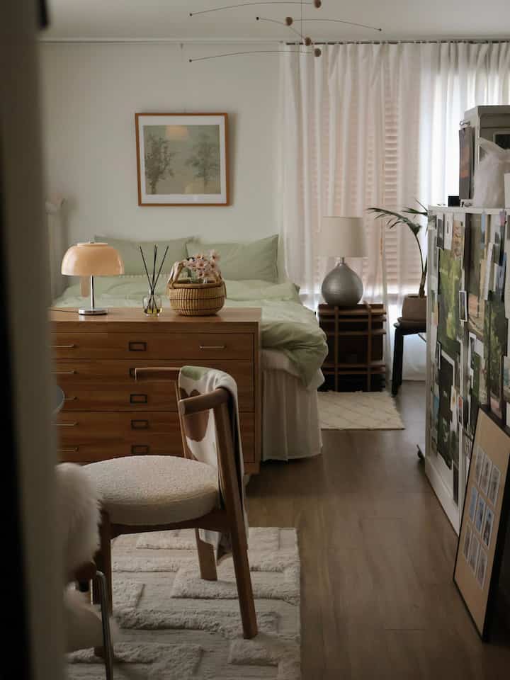 ウッドトーンとホワイト、グリーンが調和した8坪のワンルーム寝室、ベッドやチェスト、ラグ、カーテンが配置された温かみのある自然なインテリア