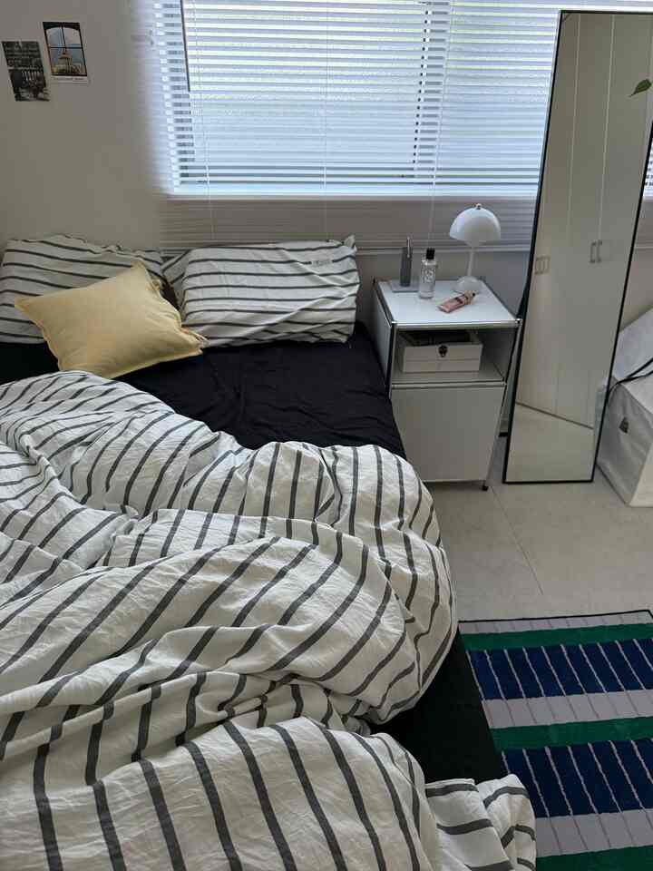 Monotone bedroom featuring striped duvet cover, white nightstand, and blinds, creating a clean atmosphere