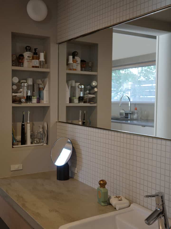 ナチュラルカラーの縦長のバスルーム、ニッチ収納と大きな鏡が配置されたミニマルな洗面スペース