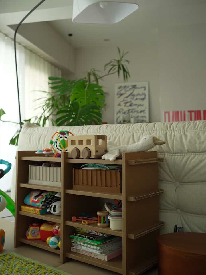 ベージュとブラウンの落ち着いた色調のリビングの一角に、赤ちゃんと子ども用の玩具収納棚が置かれた自然で雰囲気のあるインテリア