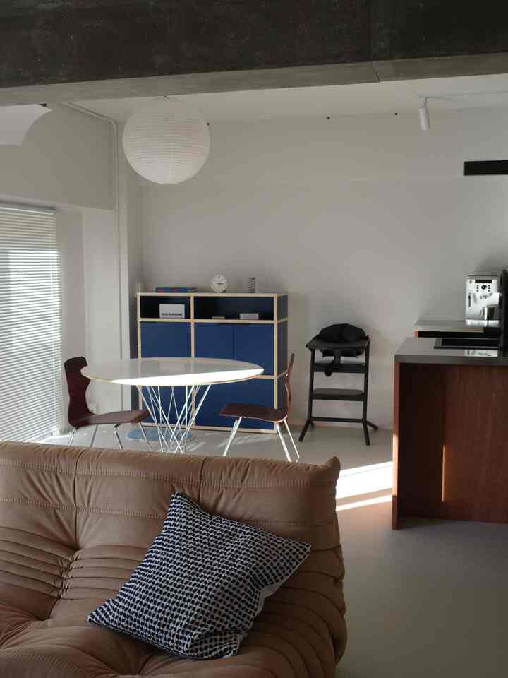 White-toned living and kitchen space featuring a brown sofa and round dining table in a modern interior