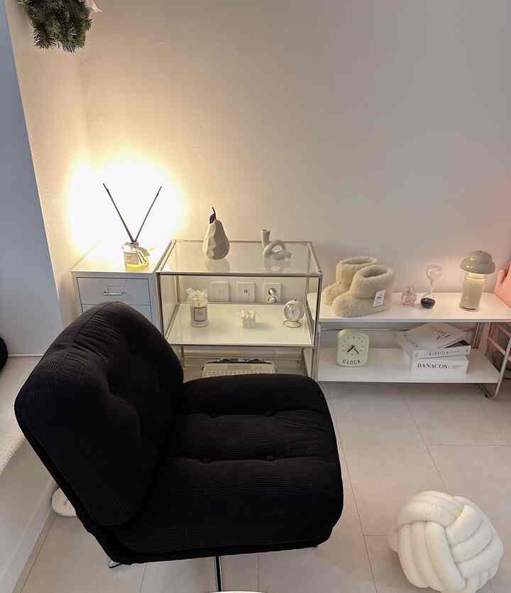 Minimalist living room in white and black tones featuring an armchair and illuminated storage shelves