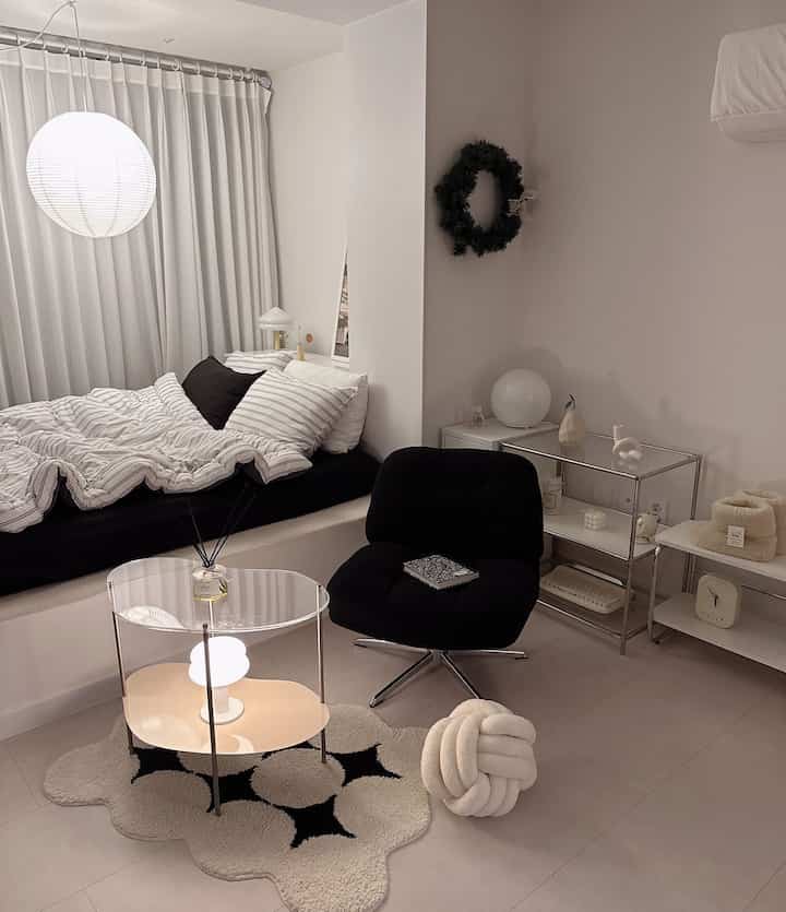 ホワイトとブラックのトーンによるミニマルな寝室、ベッド、アクリルテーブル、モダンな椅子が配置された清潔感のある空間