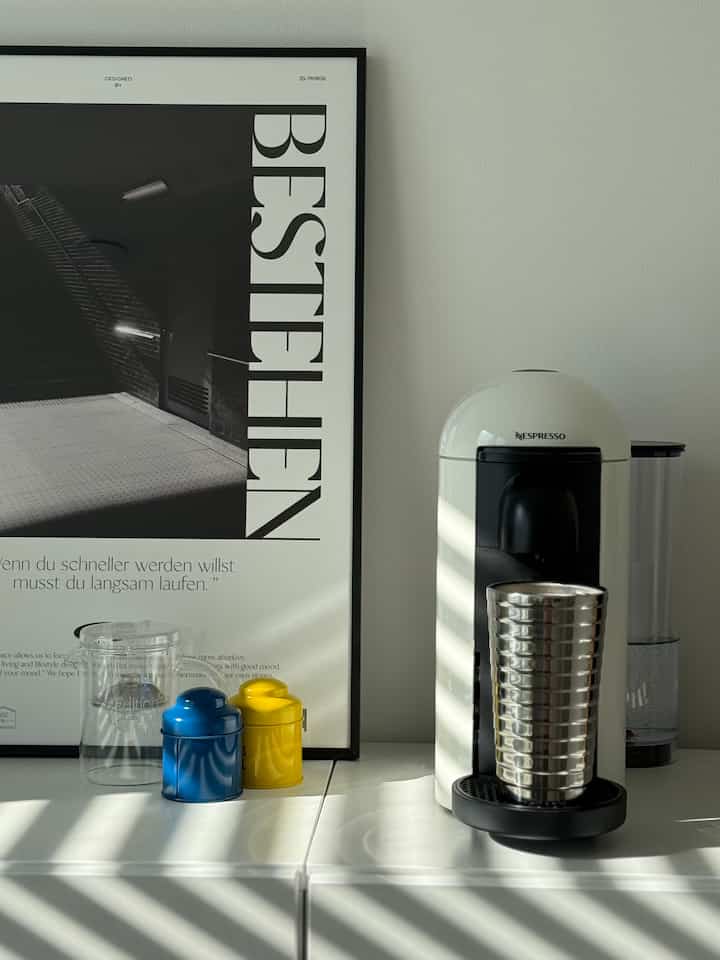 Minimal kitchen space in white and black tones featuring a Nespresso coffee machine and a poster with clean, modern decor