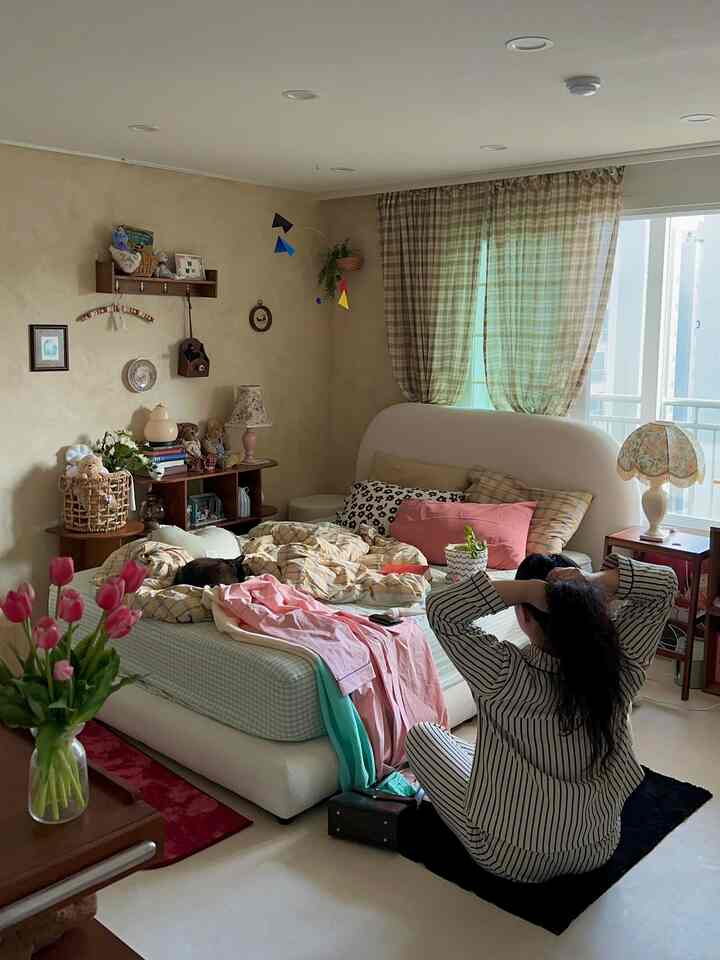 ナチュラルな木目調とホワイト、ピンク色のアクセントがある寝室、枕や掛け布団、ナイトテーブル、モビールが配置された雰囲気のあるインテリア