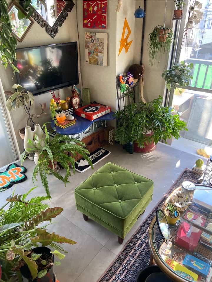 Cozy living room with green plants, mid-century modern ottoman, and a red record player near window