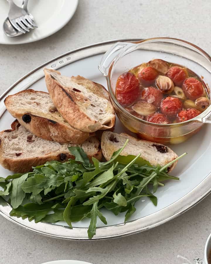 White and silver toned dining table featuring a serving plate, glass bowl of food, and cutlery arranged for a clean meal setting
