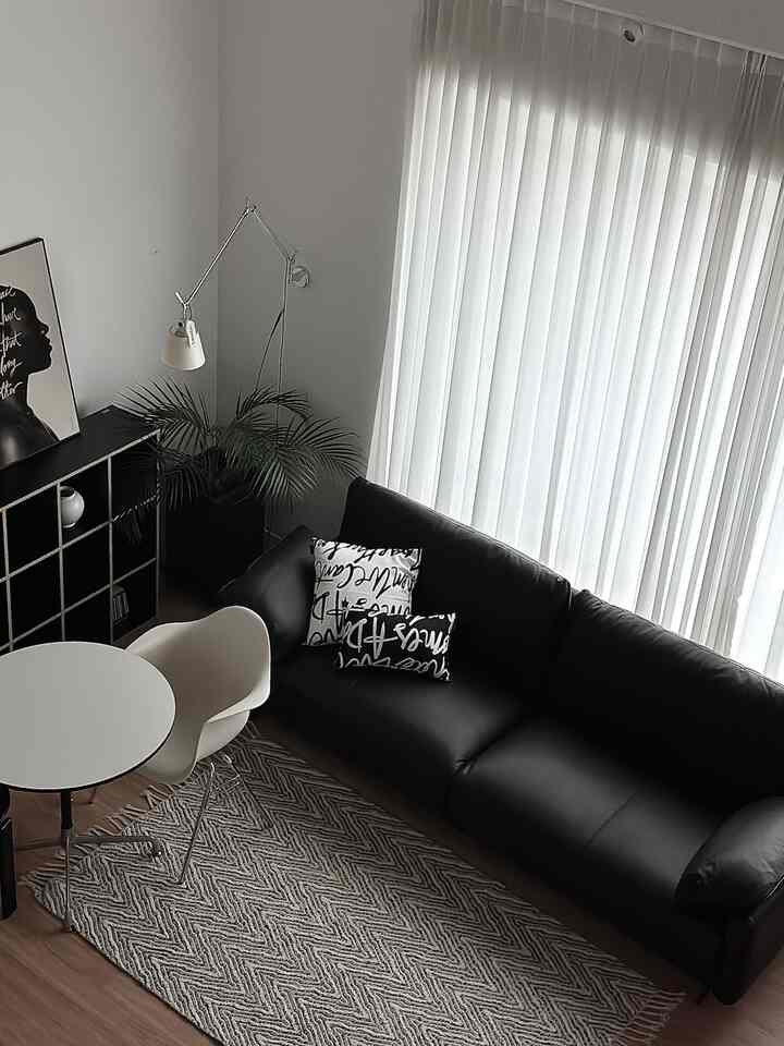 モダンで清潔感のある白いカーテンと黒いレザーソファが配置されたリビング