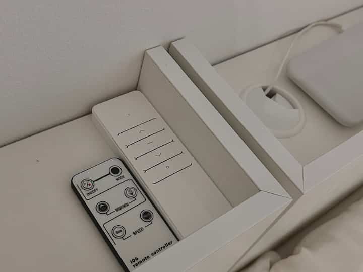 ホワイトの木目調が特徴の寝室、隙間収納を兼ねたナイトテーブルが配置された印象的な空間