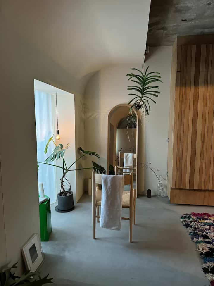 ナチュラルなベージュと木目調の玄関、シンプルな木製の椅子とアーチ型の出入口が配された落ち着いた雰囲気のインテリア