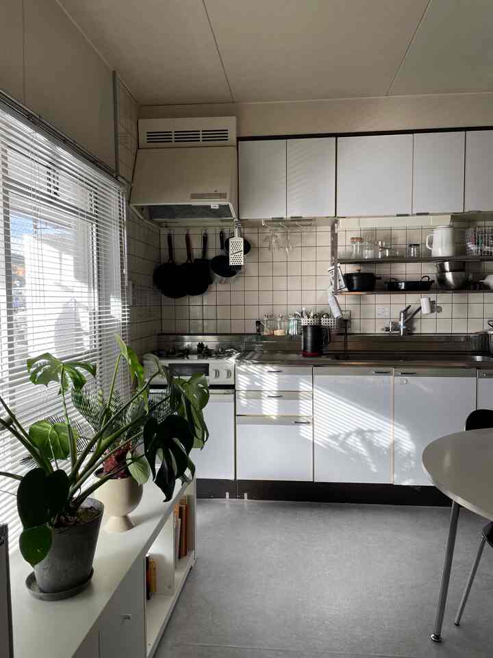 明るい朝日の差し込む白いキッチンと緑の植物が配置された清潔感のある二人暮らしの空間