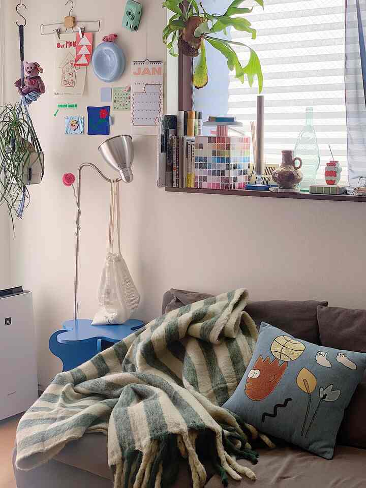 ブラウンのソファと緑のストライプのスロー、様々なウォールデコが配置されたナチュラルな色調のリビング空間