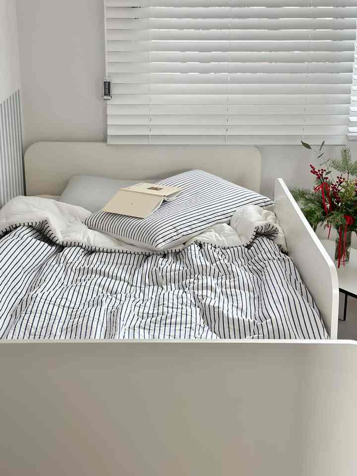 Simple children's bedroom with white and blue striped bedding, central bed frame and pillow arrangement