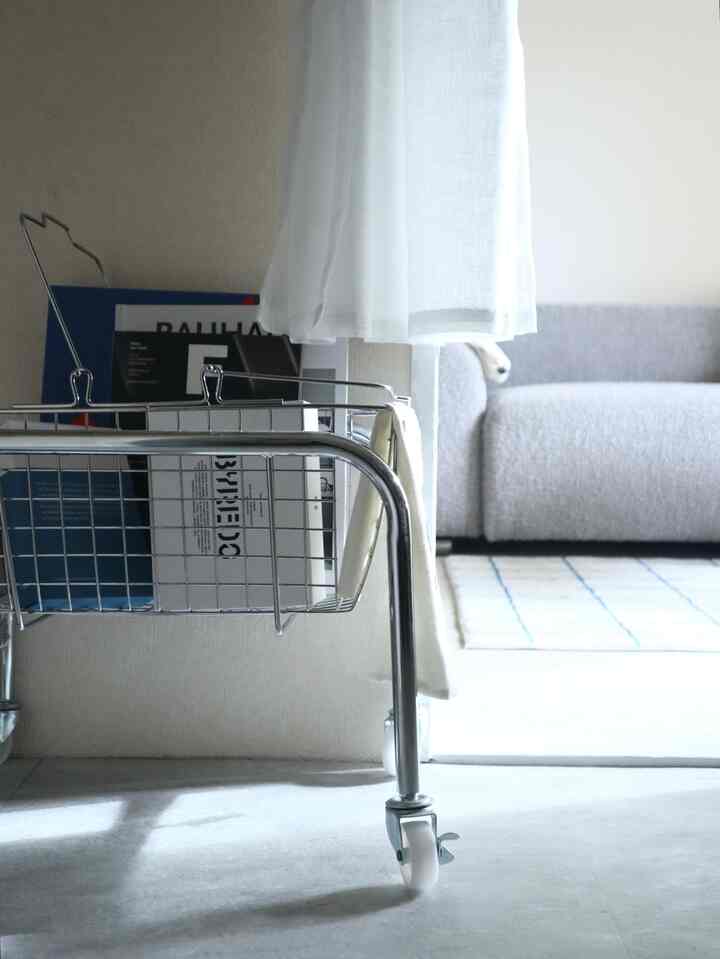 白い床とカーテンが印象的なリビングルームに、キャスター付きのメタルバスケットとグレーのソファが配置されたシンプルで清潔感のある韓国インテリア