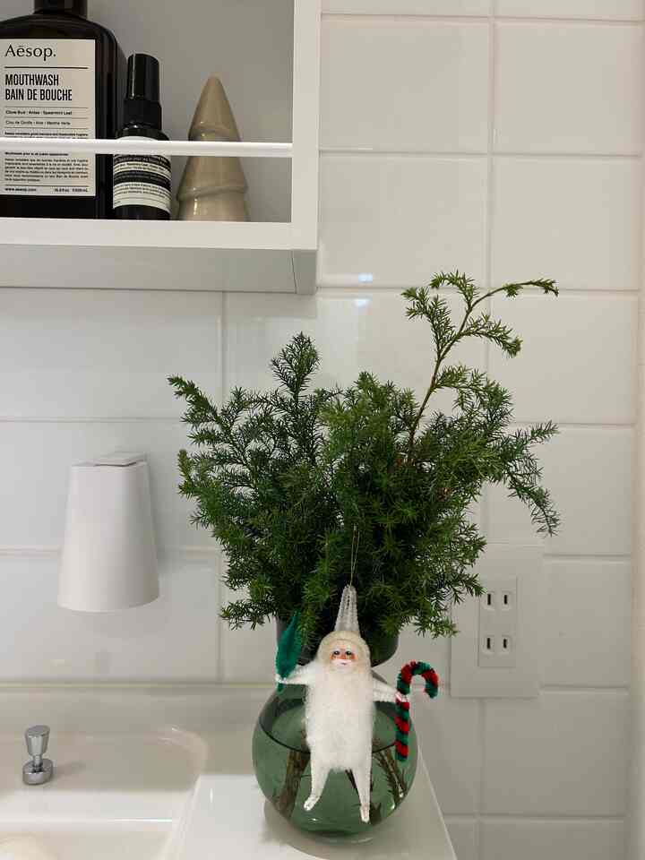 Cozy powder room corner featuring white tiled wall and bathroom sink with green vase and retro Santa objet decor