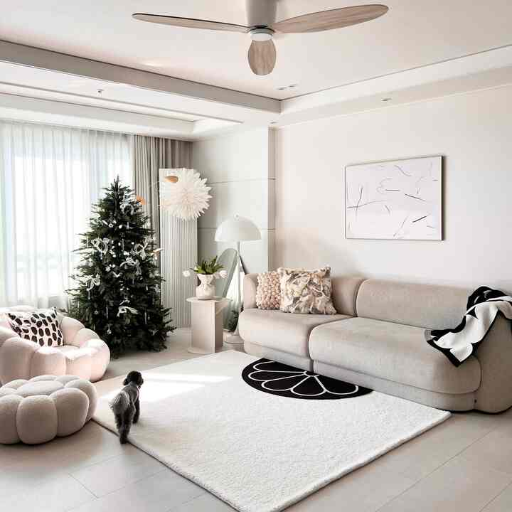 White and natural-toned living room featuring a large plush rug, beige sofa, and a decorated Christmas tree creating a warm modern atmosphere