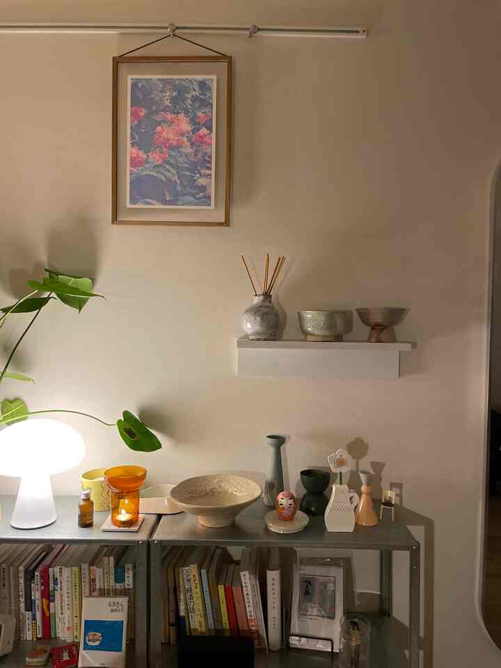 ベージュの壁に様々な陶器と額縁、植物が配置されたワンルームのインテリア