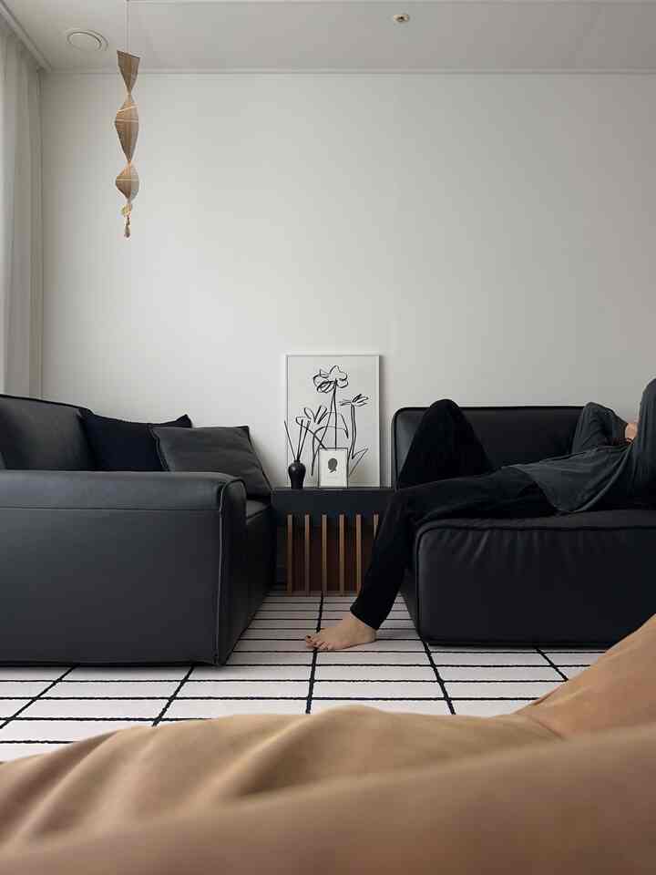 Modern living room with white walls featuring two black leather sofas and minimalist decor
