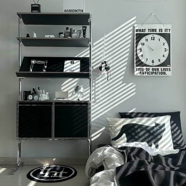 Monotone bedroom space featuring a black shelf, vintage poster clock, and black-and-white cushions and bedding for a chic interior