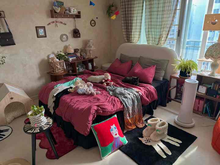 Cozy bedroom with red and black tones, featuring a large bed with various pillows and a cat resting, natural light through curtains