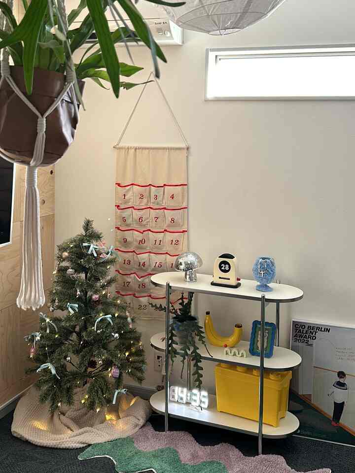 パステル調のクリスマスツリーと白い多段収納棚が配置された明るいミッドセンチュリーモダン風のリビングの一角